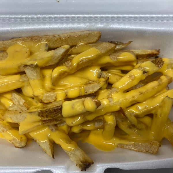 Golden french fries generously covered in melted yellow cheese sauce, served in a white takeout container.