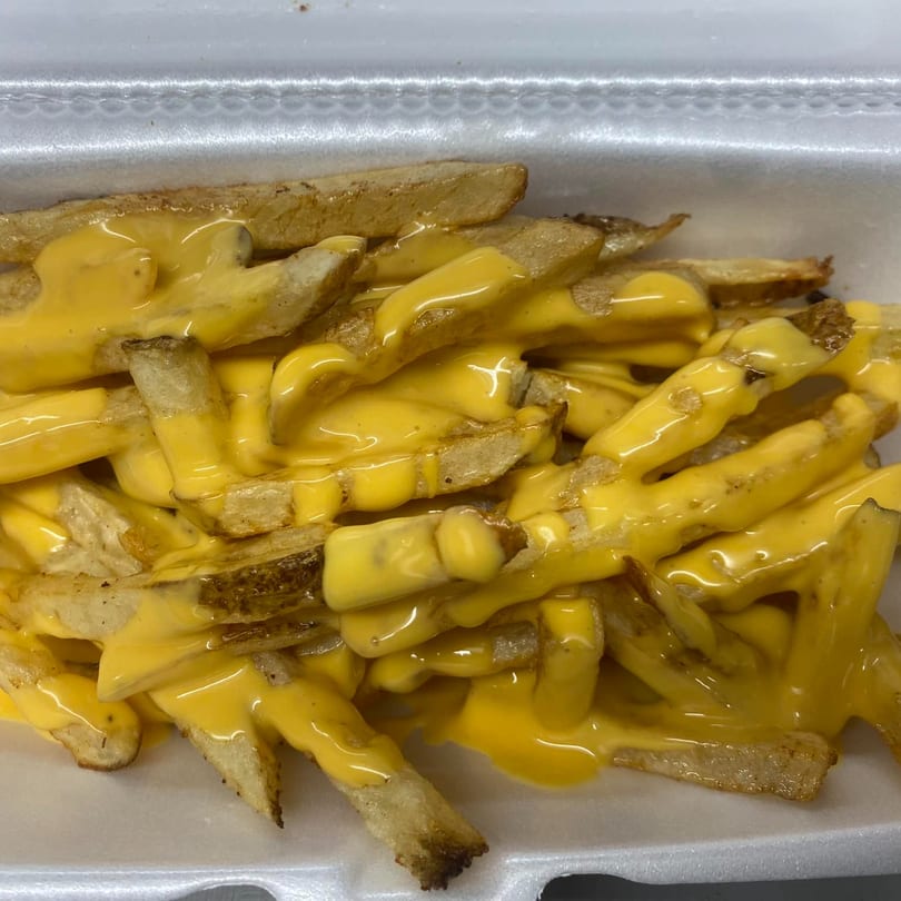Golden french fries generously covered in melted yellow cheese sauce, served in a white takeout container.