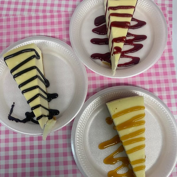 Three slices of cheesecake with chocolate, raspberry, and caramel drizzles on white plates.