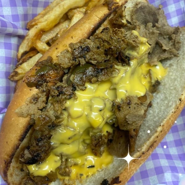 Cheesesteak with melted cheese and onions, served with a side of golden fries.