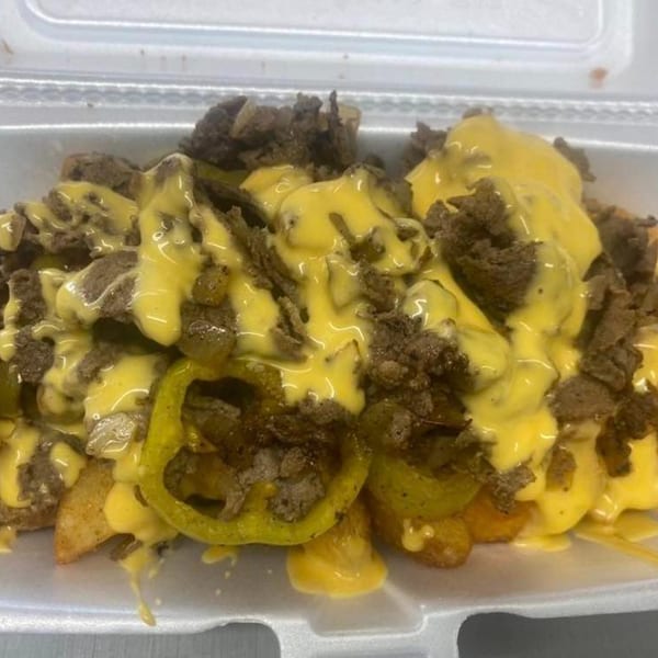 Philly Pete's cheesesteak fries, topped with melted cheese, steak, and green peppers in a white container.